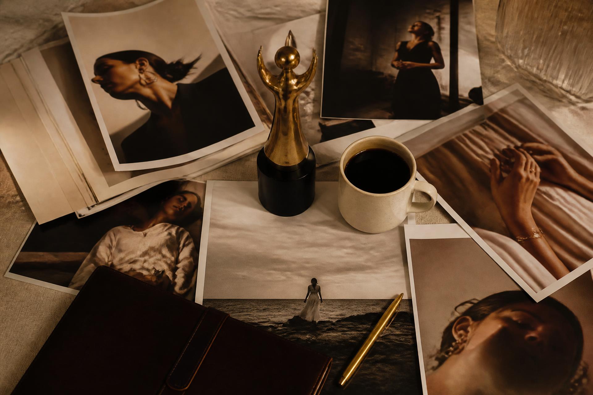 Editorial flatlay of press tearsheets, a brass award, leather portfolio, and ceramic coffee cup in warm studio light
