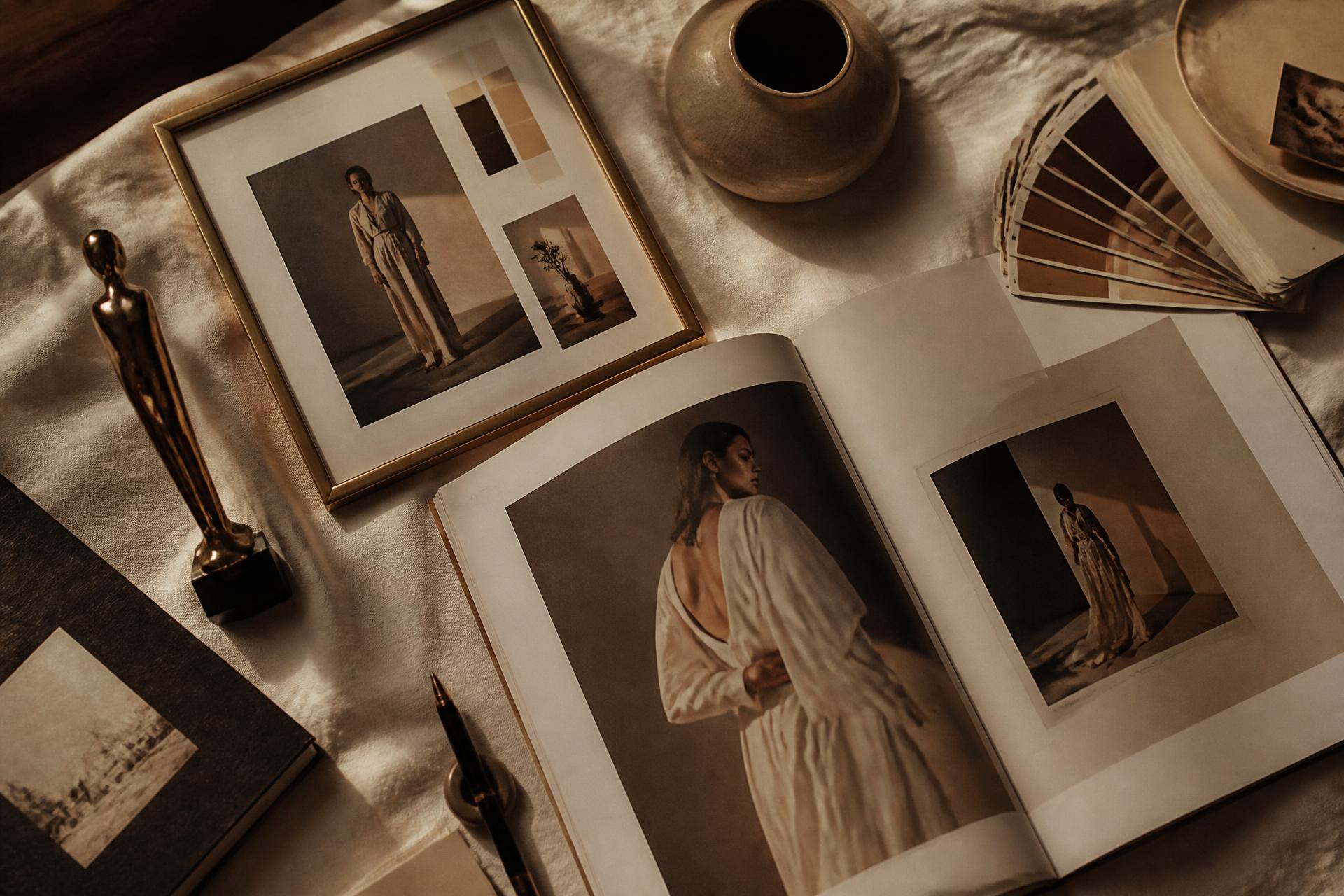 Editorial flatlay of magazine tearsheets, brass award, color swatches, and a ceramic vessel on cream linen